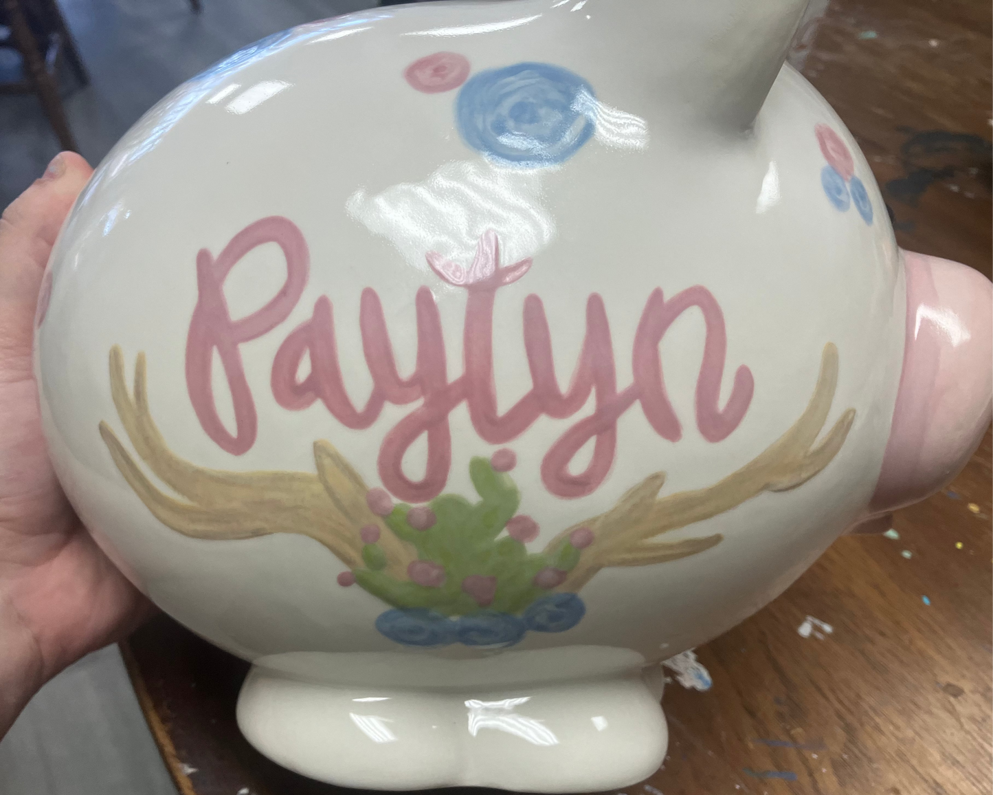 Ceramic piggy bank with 'Paylyn' and decorative elements held by a hand.