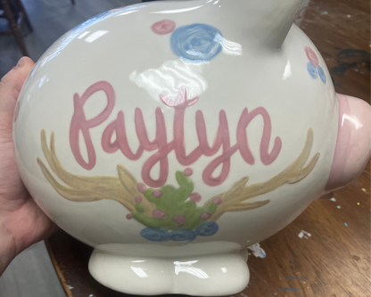 Ceramic piggy bank with 'Paylyn' and decorative elements held by a hand.