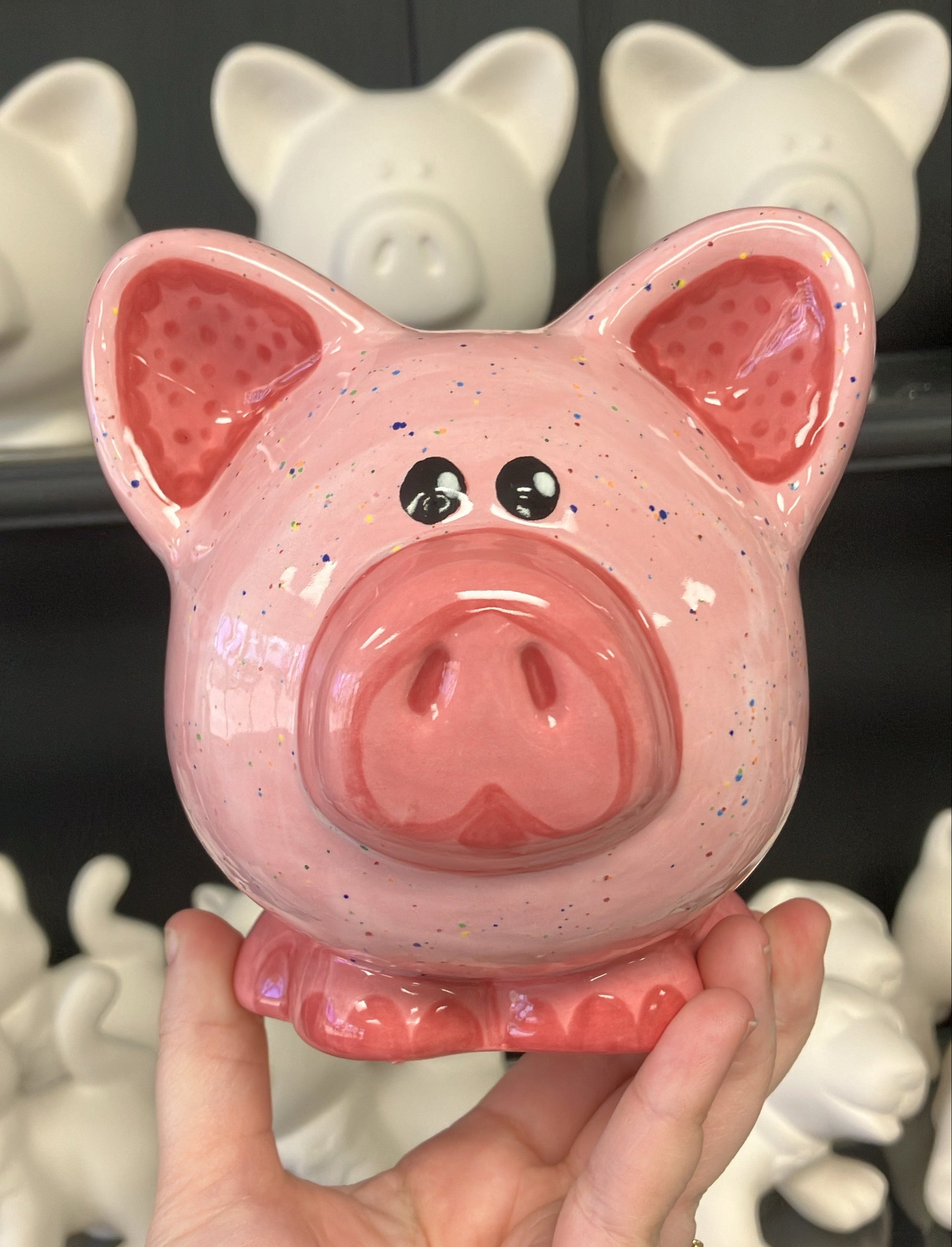 Pink piggy bank held in front of a display of similar unpainted piggy banks.